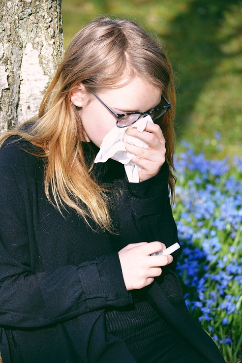 young woman suffering with allergies in the spring outside with flowers