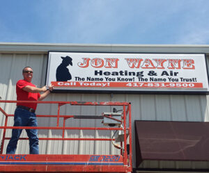 Owner of Jon Wayne Heating & Air with sign on building decades ago