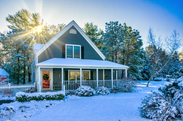 Snow covers the lawn and roof of a home as the sun shines in the background.